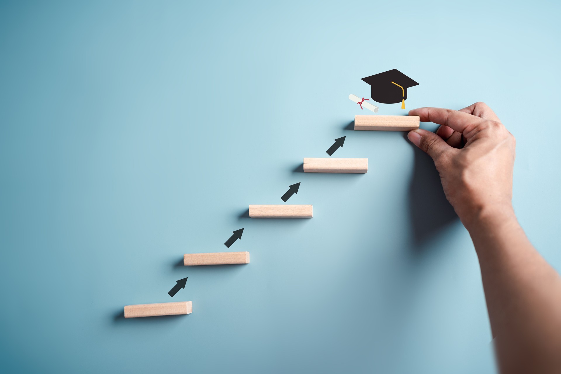 Schritte der Bildung, die zum Erfolgsziel führen. Strategische Schritte in Richtung Abschluss. Karriereweg und erste für Unternehmen, Abschlussziele-Konzept. Abschlusskappe auf Holzblock.